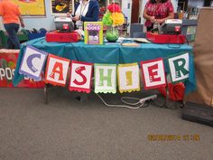 a table that has some signs on it and people in the background are standing around