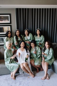 a group of women sitting on top of a couch in matching green robes and holding wine bottles