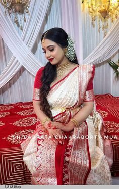 a woman sitting on top of a bed wearing a red and white sari with gold jewelry