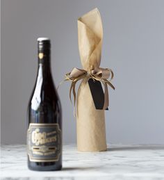 a bottle of wine next to a brown paper bag with a ribbon tied around it