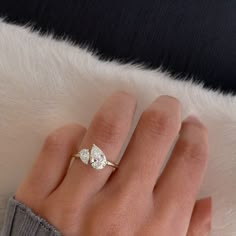 a woman's hand with a diamond ring on top of her finger and a white fur