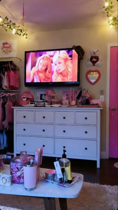 a tv that is on above a dresser in a room with pink walls and white furniture