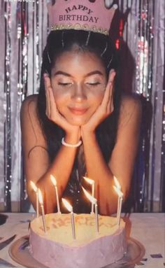 a woman sitting in front of a birthday cake with candles on it and her hands near her face