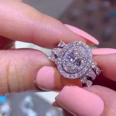 a woman's hand holding a diamond ring in her left hand, with the center stone surrounded by smaller diamonds