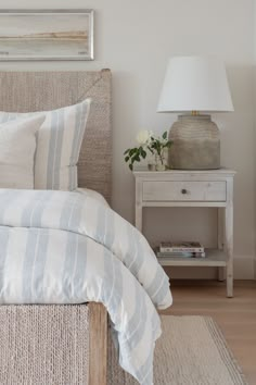 a bed with white and blue striped comforter next to a lamp on a nightstand