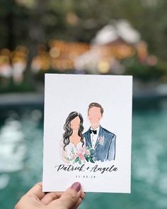 a hand holding up a wedding card with the bride and groom in water behind them