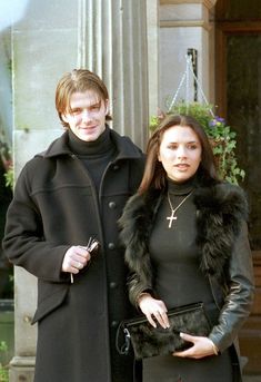 a man and woman standing next to each other in front of a building with flowers