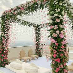 an outdoor wedding setup with white and pink flowers on the arch over looking the ocean