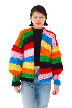 a woman standing in front of a white background wearing a multicolored knitted jacket