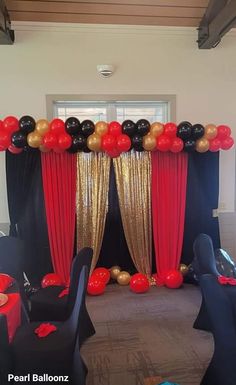 a party room with black and red balloons on the wall, gold drapes and curtains