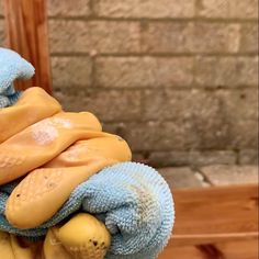 a pile of blue and yellow towels sitting on top of a wooden chair next to a brick wall