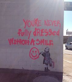 a graffiti on the side of a building that says, you're never fully dressed when a smile