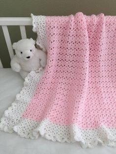 a crocheted pink and white blanket next to a teddy bear on a bed