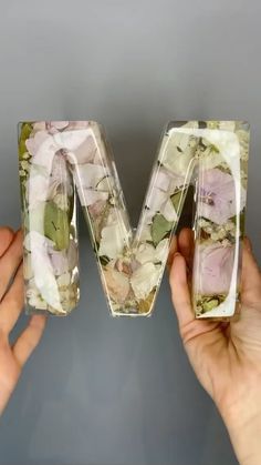 two hands holding up the letter m made out of flowers and plastic wrap around it