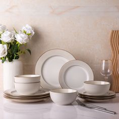 a table with white dishes and flowers in vases on top of it, along with silverware