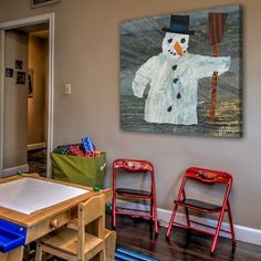 there is a painting on the wall and two chairs in front of it, with a snowman painted on the wall