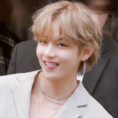 a young man in a suit and necklace smiles at the camera while standing next to other people