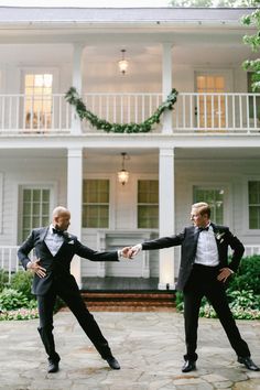 two men in tuxedos are dancing on the ground near a large white house