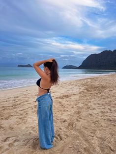 a woman standing on top of a sandy beach next to the ocean with mountains in the background