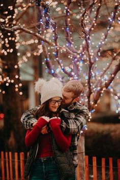 a man and woman hugging in front of a tree with christmas lights on the branches