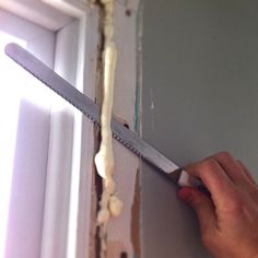 a person with a pair of scissors cutting through the side of a wall that has been painted white