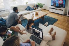 group of people sitting on couches with laptops in front of them, watching television