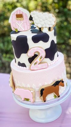 a three tiered cake decorated with farm animals and numbers on the top, sitting on a purple table cloth