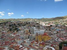 an aerial view of a city with buildings and mountains in the backgrouds