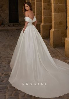 a woman in a white wedding dress standing on a cobblestone walkway with her back to the camera