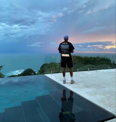 a man standing on the edge of a swimming pool looking out at the ocean and clouds