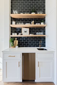 a kitchen with white cabinets and black tile backsplash, open shelving above the sink