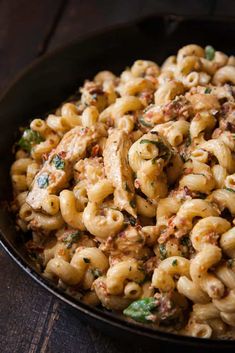 a black bowl filled with macaroni salad on top of a wooden table next to a fork