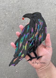 a hand holding a paper mache of a black bird with multicolored feathers