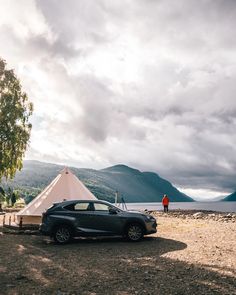 a car parked in front of a teepee next to a body of water with mountains in the background