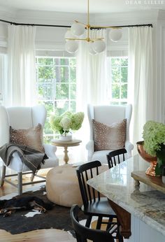 two white chairs sitting in a living room next to a table with flowers on it