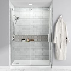 a white tiled bathroom with a walk in shower next to a towel rack and robe hanging on the wall