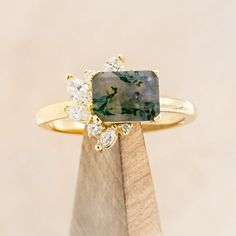 a yellow gold ring with a green and white stone surrounded by three small round diamonds