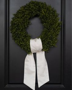 a wreath is hanging on the front door with a white scarf around it's neck