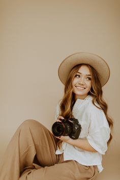 a woman sitting on the floor with a camera in her hand and wearing a hat