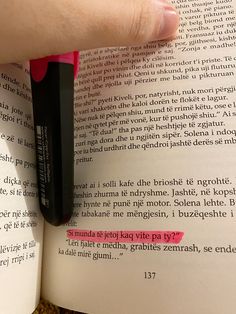 a person is holding a pen over an open book with pink writing on it and the pages are black