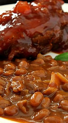 a white plate topped with beans and meat covered in sauce next to a green leaf