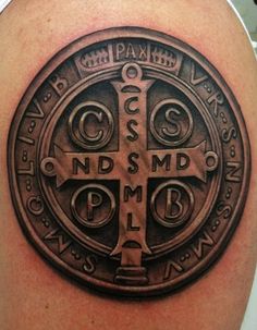 a cross tattoo on the back of a man's upper half arm, with words and symbols around it