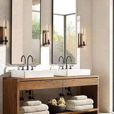 two sinks and mirrors in a bathroom with towels on the shelf under them next to each other