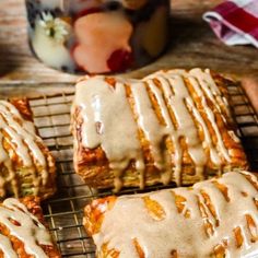 cinnamon rolls with icing sitting on a cooling rack next to apples and a cup of coffee