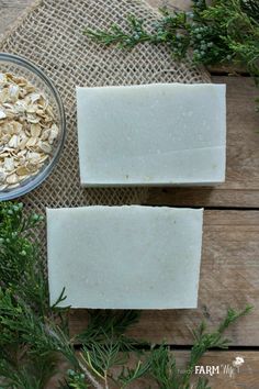 two bars of oatmeal soap sitting on top of a wooden table next to a bowl of oats