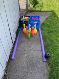 an outdoor bowling game set up on the sidewalk next to a fence with balls in it