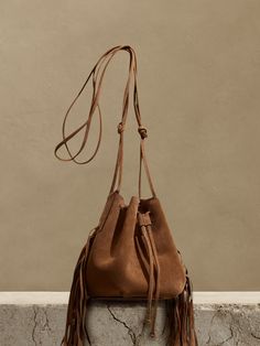 We updated our best-selling bucket bag, adding fringed leather accents and increasing storage space to accommodate even the largest phones.  Handcrafted in Italy of Italian suede.  Drawstring closure.  Adjustable shoulder strap.  Height: 7" (18cm) Diameter: 7" (18cm) Strap drop: 25" (38cm) Suede Bucket Bag For Travel, Suede Bucket Bag With Removable Pouch, Suede Bucket Shoulder Bag With Removable Pouch, Suede Bucket Bag With Adjustable Strap For Travel, Suede Bucket Bag With Removable Pouch For Travel, Travel Suede Bucket Bag With Adjustable Strap, Suede Bucket Bag With Adjustable Strap, Suede Shoulder Bucket Bag With Adjustable Strap, Crossbody Bucket Bag With Tassels For Travel