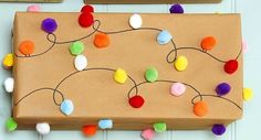 a cardboard box decorated with colorful pom - poms and twine of string lights