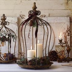 two metal birdcages filled with pine cones and lit candles on top of a table