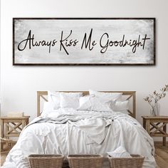 a bed with white sheets and two baskets on the headboard, next to a wooden sign that says always kiss me goodnight